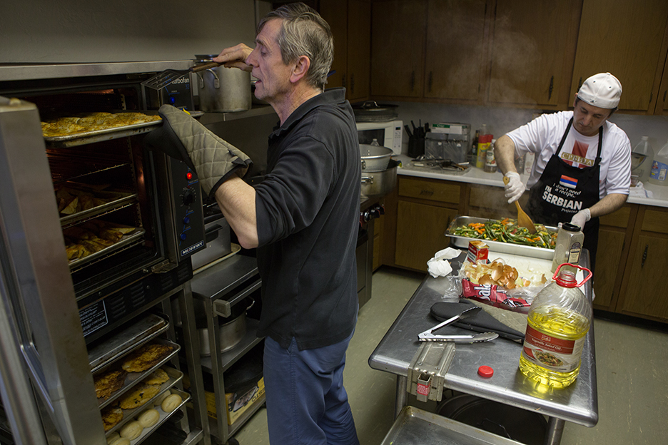 One man checks on fish in an oven, while another prepares vegetables